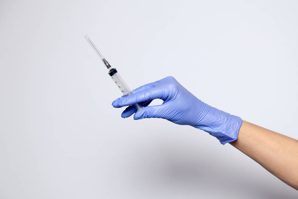 Closeup doctor's hand in rubber purple glove holding transparent syringe with closed cap. Isolated on white background. Concept of rejection of vaccinations, vaccination, rabies injection - Photo, Image