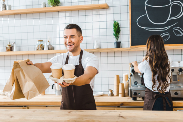 apuesto cajero sosteniendo papel tazas y bolsas wile atractivo morena barista haciendo café en café casa
 - Foto, imagen
