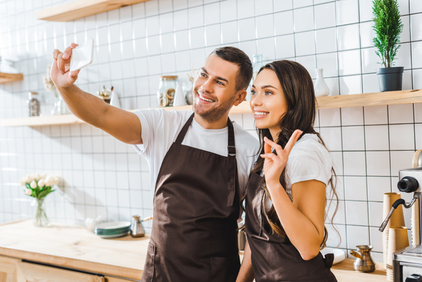 cashiers in aprons standing near bar counter and taking selfie in coffee house - Photo, Image