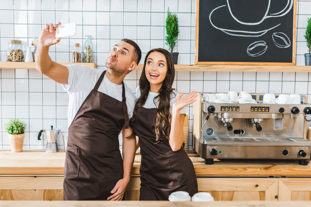 Pokladníci v hnědé zástěry stojí a s selfie v kavárně - Fotografie, Obrázek