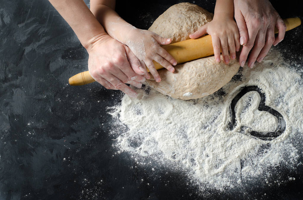 Mother and children hands rolled dough with a rolling pin on the black table. Top view. - Φωτογραφία, εικόνα