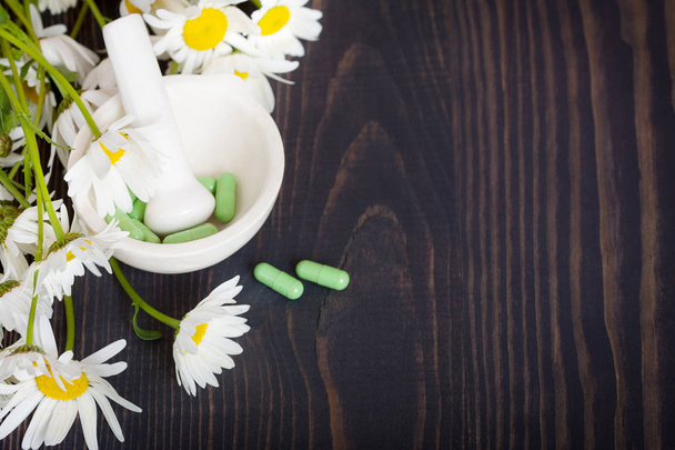Flores de manzanilla y cápsulas fitoterapéuticas verdes sobre una mesa de madera. Medicina herbal y salud
 - Foto, imagen