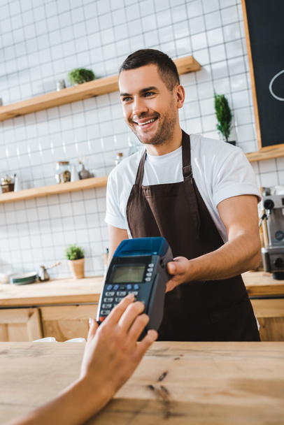 handsome cashier standing near bar counter and holding terminal wile woman making transaction in coffee house - Photo, Image