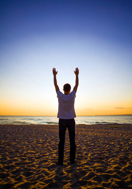 Ihmisen siluetti rukoilee auringonlaskussa meren taustalla
 - Valokuva, kuva
