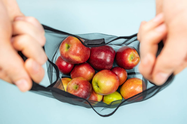 Holding a reusable string bag full of apples. Sustainable eco packaging concept: shopping for groceries with a multi-use bag to reduce ecological footprint - Фото, изображение