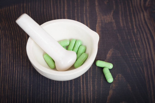 Farmácia pilão e argamassa com cápsulas verdes em uma mesa de madeira
. - Foto, Imagem