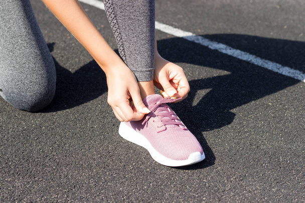 Meisje liggen op zijn roze sneakers voor hardlopen. geen gezicht close-up. Buitenlucht en zonlicht, stadion, sport, fitness concept. - Foto, afbeelding