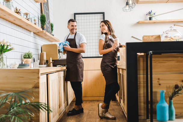 barista and cashier standing behind bar counter in coffee house - Photo, Image