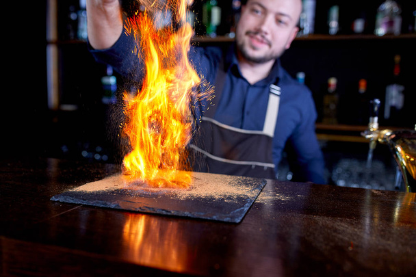 Fiery show at the bar. The bartender makes hot alcoholic cocktail and ignites bar. Bartender prepares a fiery cocktail. Fire on bar. - Photo, Image
