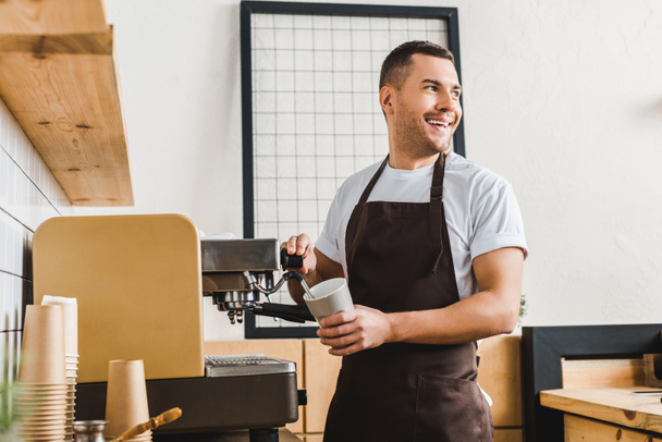 hezký barista drží pohár a přípravu kávy se strojem v kavárně - Fotografie, Obrázek