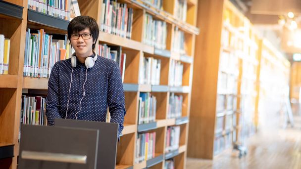 Junger asiatischer Universitätsstudent schiebt Bücherwagen in College-Bibliothek und findet Lehrbücher für die Bildungsforschung. Bestsellersammlung im Buchhandel. Stipendien oder Konzepte für Bildungschancen - Foto, Bild