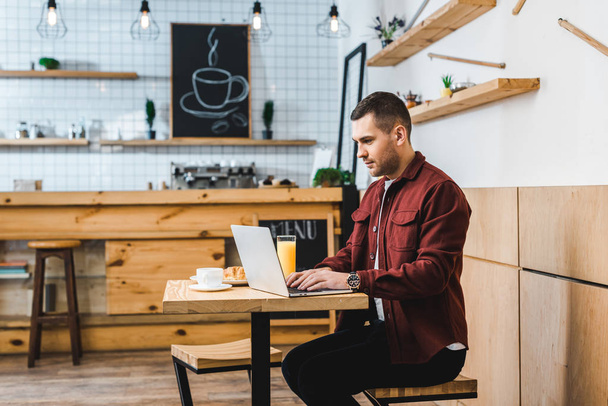 handsome freelancer sitting at table with laptop in coffee house - Photo, Image
