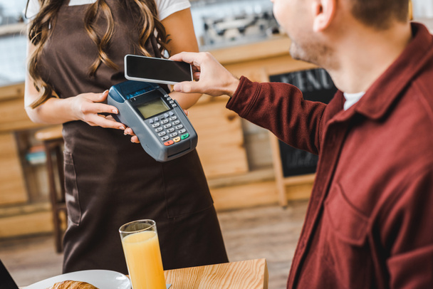 waitress view of barista holding terminal wile freelancer at table paying with smartphone in coffee house - Photo, Image