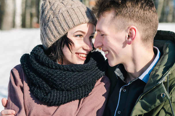 Mooie jonge verliefde paar knuffelen in het park op een heldere zonnige winterdag. Jongen en meisje glimlach bij elkaar, close-up - Foto, afbeelding