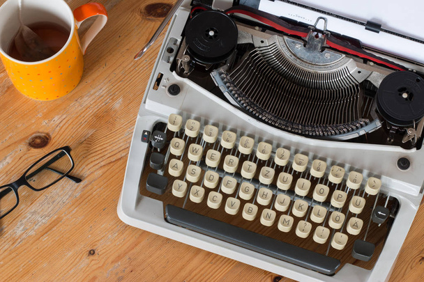 Vintage typewriter, glasses and cup of coffee on a wood desk - Fotó, kép