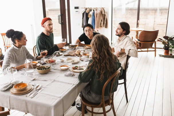 Giovani amici internazionali seduti a tavola pieni di cibo che sognano di parlare tra loro. Gruppo di colleghi che trascorrono del tempo insieme a pranzo in un accogliente caffè
 - Foto, immagini