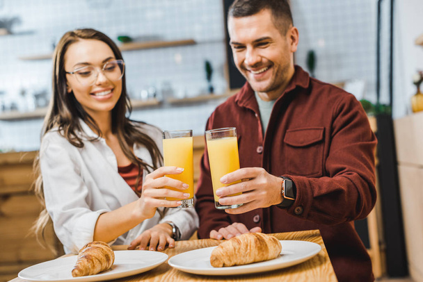 foco selectivo de vasos con jugo en manos de hombre y mujer sentados a la mesa con croissants en cafetería
 - Foto, imagen
