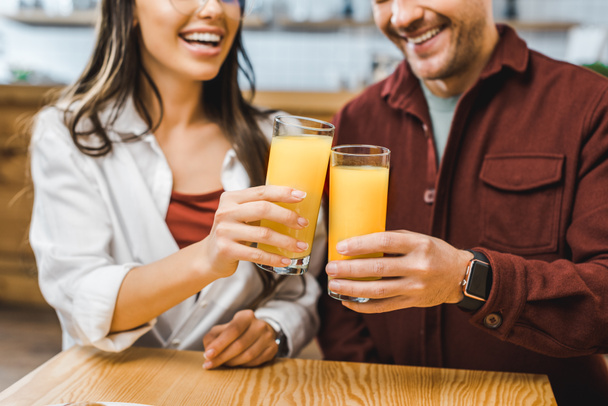 vista ritagliata di donna e uomo seduti a tavola e bicchieri di clinking con succo di frutta in caffetteria
 - Foto, immagini