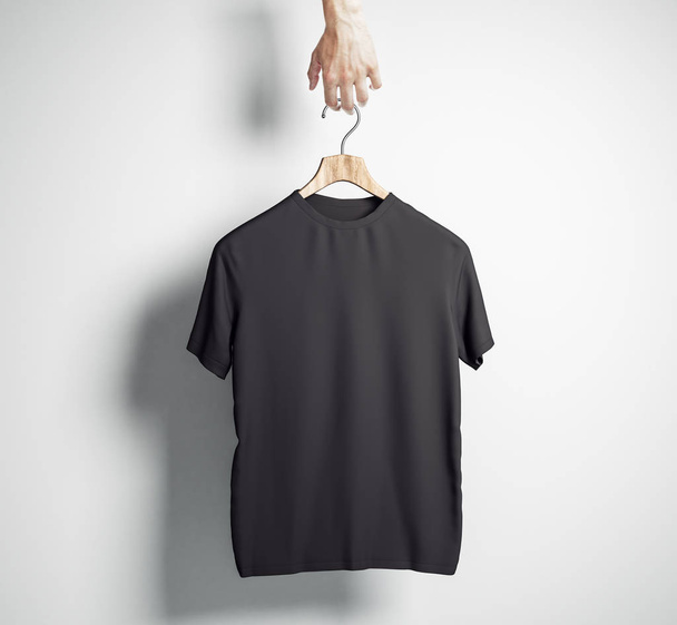 Hand holding hanger with empty black t-shirt on concrete wall background. Design and shop concept. Mock up, 3D Rendering  - 写真・画像