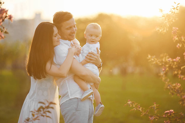 Beautiful young parents and their cute little son hugging and smiling at the sunset - Fotografie, Obrázek