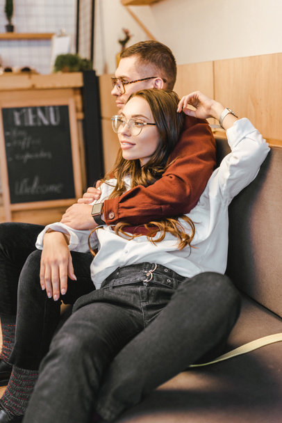 attractive woman and man in glasses sitting on couch and hugging in coffee house - Fotó, kép