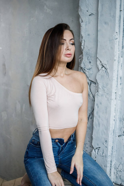 Portrait of beautiful young woman in blue jeans and beige t-shirt. Young model standing close to wall at luxury apartments interior - Foto, Imagen