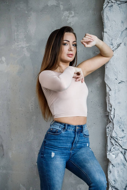 Portrait of beautiful young woman in blue jeans and beige t-shirt. Young model standing close to wall at luxury apartments interior - Foto, afbeelding