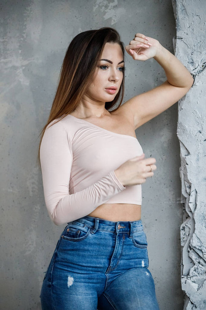 Portrait of beautiful young woman in blue jeans and beige t-shirt. Young model standing close to wall at luxury apartments interior - Foto, Imagem