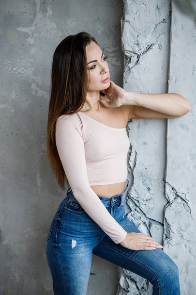 Portrait of beautiful young woman in blue jeans and beige t-shirt. Young model standing close to wall at luxury apartments interior - Foto, afbeelding