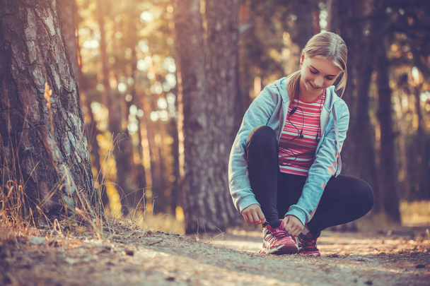 woman Runner tying shoelaces on sneakers. Morning jogging in the forest. Fitness - Photo, Image