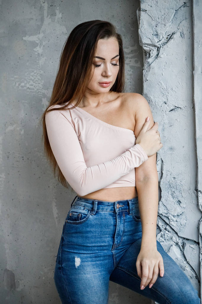 Portrait of beautiful young woman in blue jeans and beige t-shirt. Young model standing close to wall at luxury apartments interior - Foto, imagen