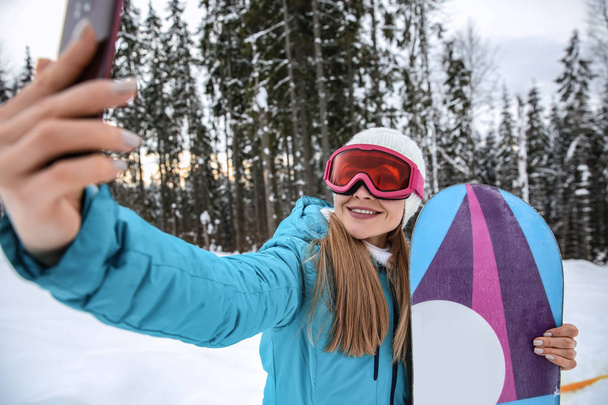 Sportieve vrouw die selfie met snowboard in winter resort - Foto, afbeelding