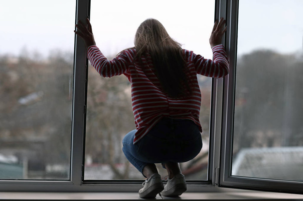 Молодая женщина собирается покончить жизнь самоубийством у окна
 - Фото, изображение