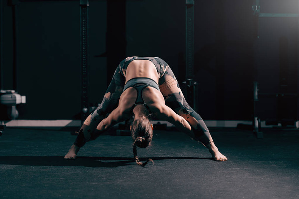 kaukasische muskulöse sportliche Frau mit Zopf Stretching in der Turnhalle. Nacht-Workout-Konzept. - Foto, Bild