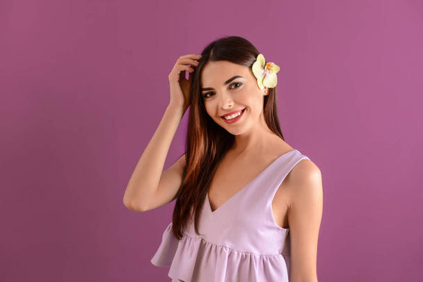schöne junge Frau mit Orchideenblume auf farbigem Hintergrund - Foto, Bild
