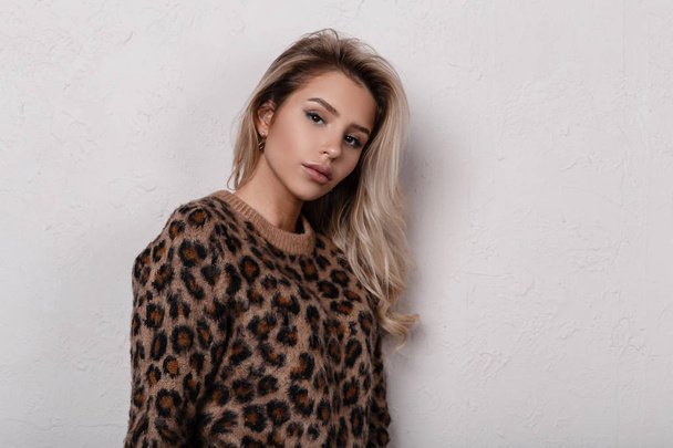 Portrait of lovely cute young woman with beautiful eyes with natural make-up with sexy lips in a stylish leopard sweater on a white background. Charming sensual girl blonde. - 写真・画像