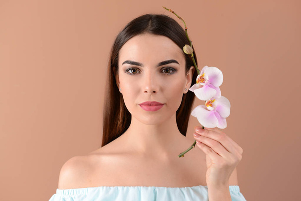 Beautiful young woman with orchid flowers on color background - Foto, Imagen