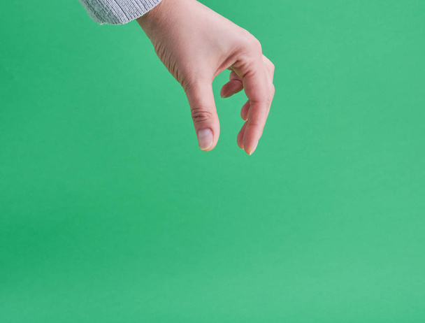 γυναικείο χέρι δείχνοντας χειρονομία του κρατώντας ένα αντικείμενο σε πράσινο φόντο - Φωτογραφία, εικόνα