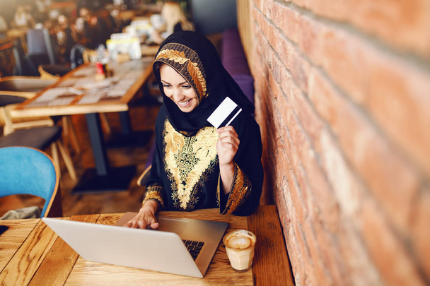 Felülnézet toothy mosollyal gyönyörű muszlim nő öltözve hagyományos viselet használ laptop on-line vásárlási kávézóban ülve. A kávé asztal. - Fotó, kép