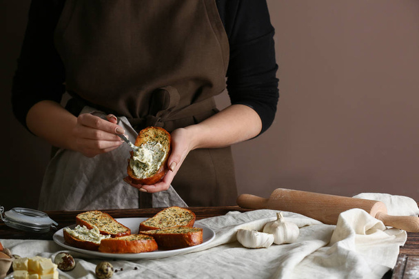 Woman spreading tasty garlic bread with cheese in kitchen - Photo, Image