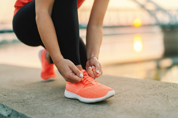 sportieve vrouw koppelverkoop schoenveter terwijl knielend buiten, In de achtergrond brug. Fitness buitenshuis concept. - Foto, afbeelding