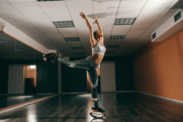 Beautiful fit Caucasian brunette in sportswear jumping on kangoo jumps footwear in gym. - Fotoğraf, Görsel
