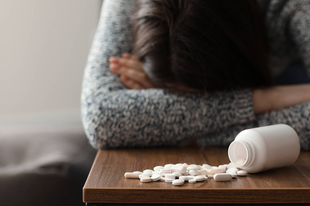 Depressed woman near heap of pills on table at home - 写真・画像
