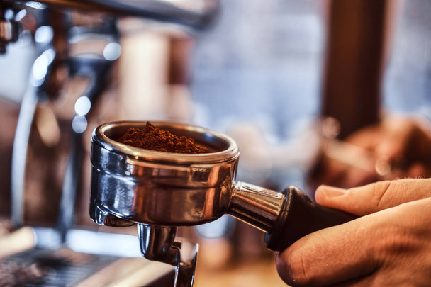 Nahaufnahme einer Hand, die einen Portafilter mit schwarzem gemahlenem Kaffee in einem Café oder Restaurant hält - Foto, Bild