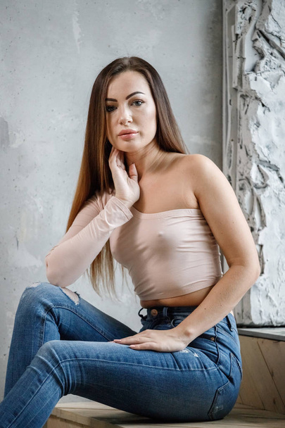Portrait of beautiful young woman in blue jeans and beige t-shirt. Young model sitting on floor at luxury apartments interior - Foto, Bild