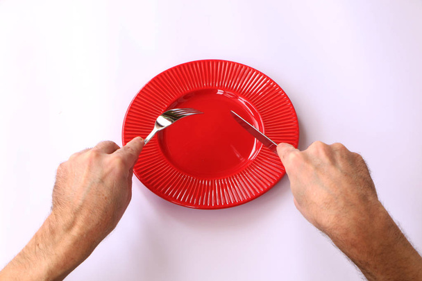 Close-up - red plate on a white background. In his hand a knife and fork. - Фото, изображение