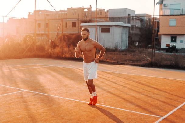 Shirtless Καυκάσιος γενειοφόρος άνδρας τρέχει στο γήπεδο το πρωί το καλοκαίρι. - Φωτογραφία, εικόνα