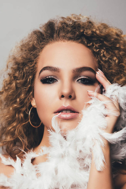 Close view portrait of young curly woman with stylish makeup and feathers in hands - Fotó, kép