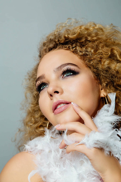 Close view portrait of young curly woman with stylish makeup and feathers in hands - Foto, Imagem