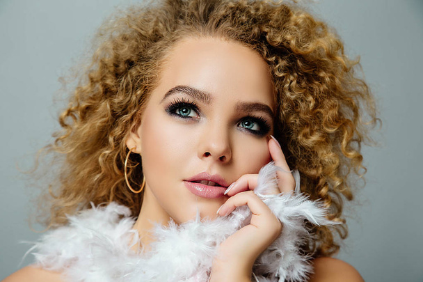 Close view portrait of young curly woman with stylish makeup and feathers in hands - Foto, imagen